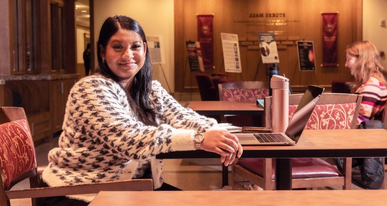 student in Bapst Library at a laptop, with other students at tables studying in the background